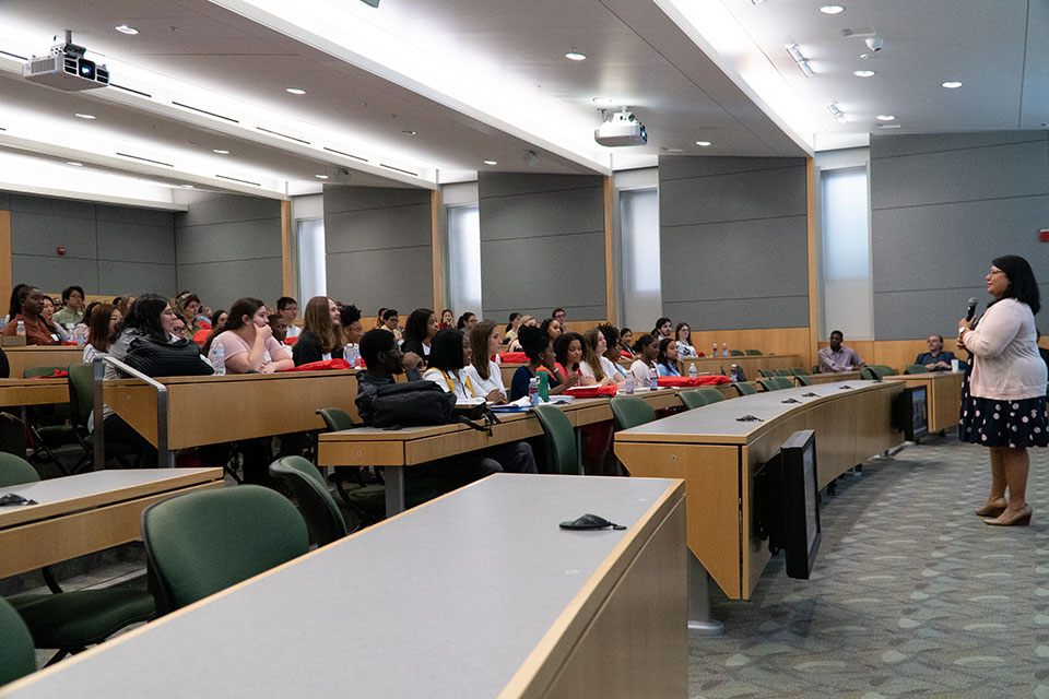 Dr. Cherokee Layson-Wolf stands at the front of a lecture hall addressing students seated in the audience.