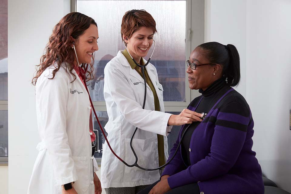 Two pharmacists listen to a patient's heart.