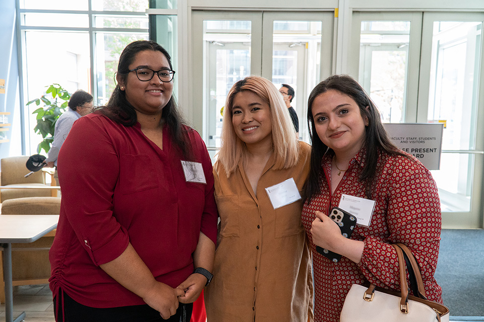 Three students smile inside the Pharmacy Hall entrance.