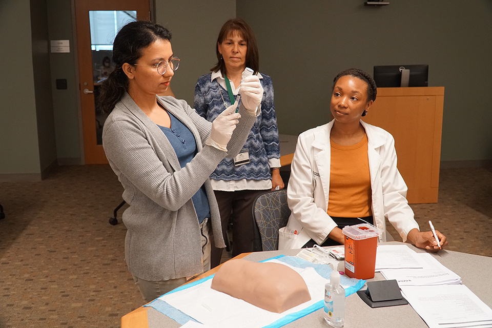 A professor watches as students work with a syringe.